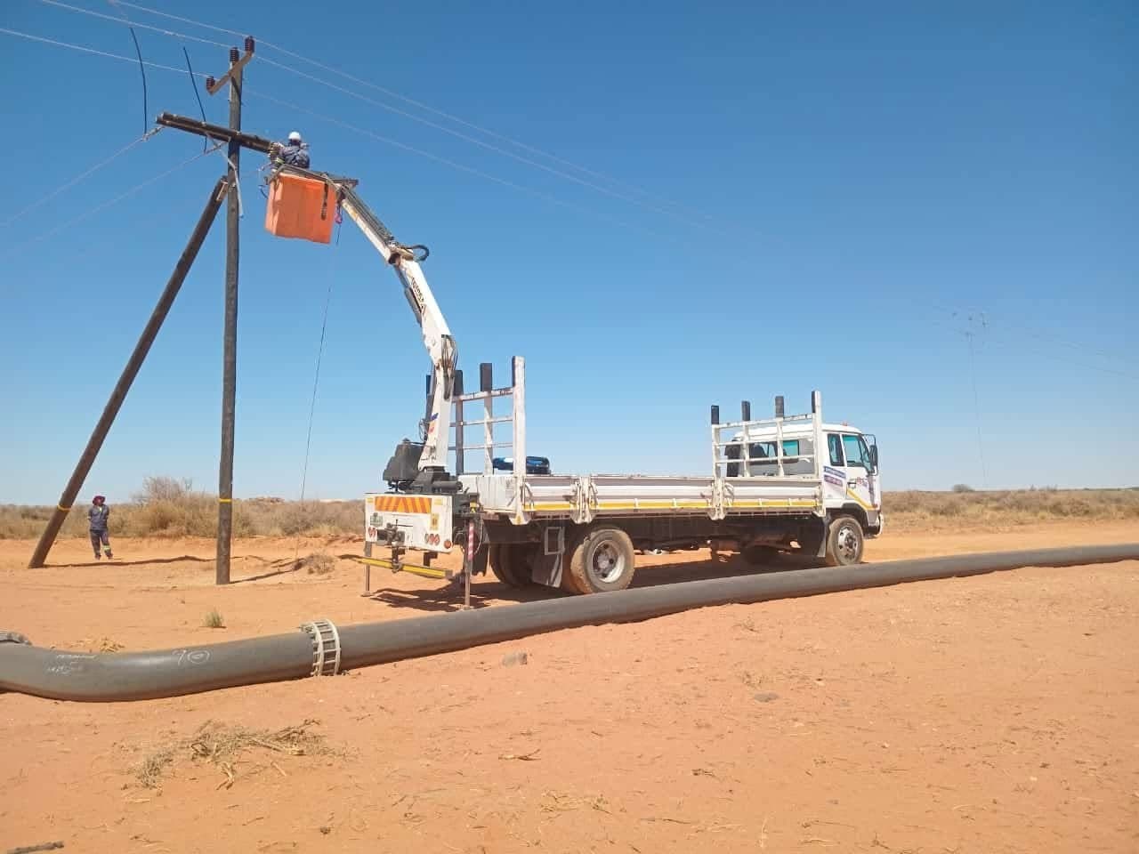 Cherry picker truck lifting a linesman to the top of a pole structure on an overhead line in red Kalahari sand