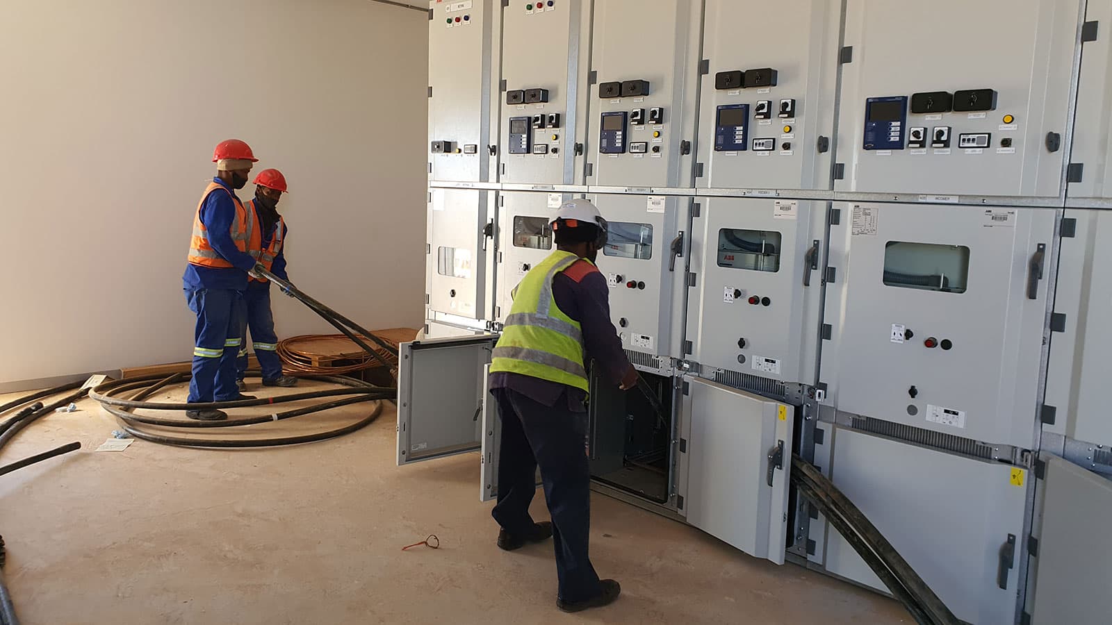 Electricians pulling medium-voltage cable into ABB switchgear panels inside a newly built substation building